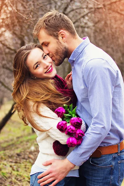 Glückliches Paar zusammen. Porträt eines bärtigen Mannes, der seine schöne Freundin mit Blumen im Garten küsst. — Stockfoto