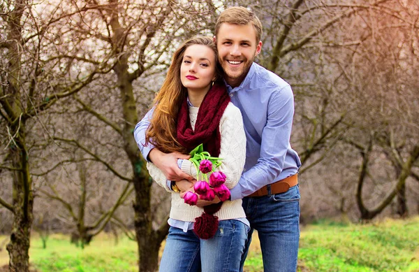 Happy grupp. Porträtt av skäggig man står bakom hans flickvän och kramar henne. Vackra leende unga par på trädgården. — Stockfoto