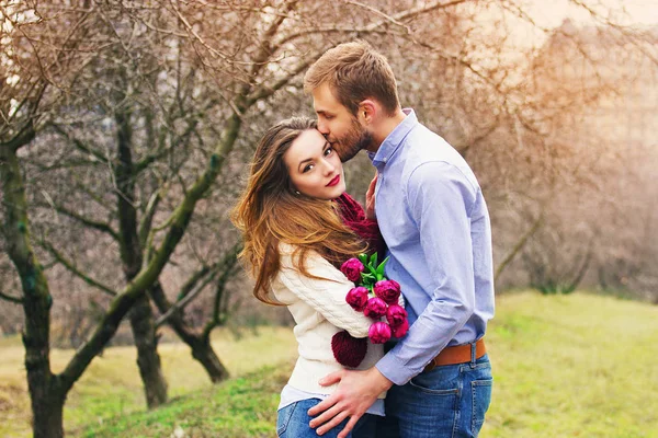 Glücklich zusammen. Porträt eines bärtigen Hipsters, der seine Freundin küsst, die Blumen in der Hand hält. Schönes junges Paar im Garten. — Stockfoto