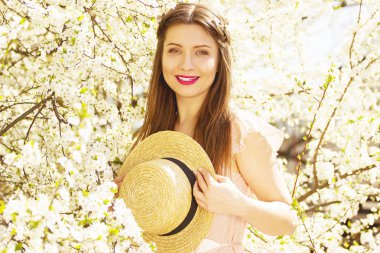 Çiçekler her yerde vardır. Güzel gülümseyen portresi ve çiçek arka plan üzerinde duran ve şapka tutmak uzun saçlı kız.