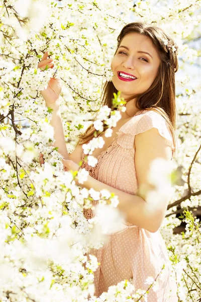 부드러운, 웃는 젊고 아름 다운 긴 머리 소녀 꽃 배경에 서 있는 핑크 드레스에의 꽃. — 스톡 사진