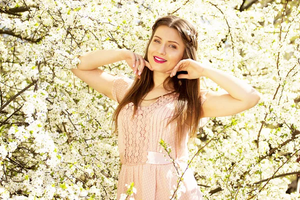 Blomma porträtt av anbud, leende ung och vacker långhårig flicka i rosa klänning står på blomma bakgrund. — Stockfoto