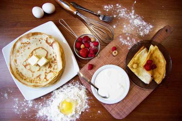 Vista de close-up superior de panquecas com frutas, creme de leite e manteiga em pratos. Morango, framboesa e ovos na farinha ingridients no fundo de madeira . — Fotografia de Stock