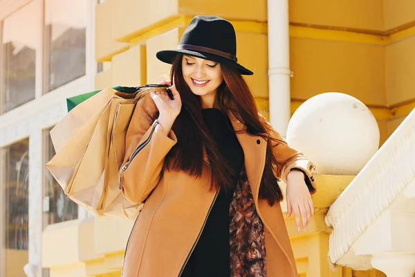 Šťastná dívka. Portrét krásné dívky v klobouk a béžový kabát těší její nákupní dobu podržíte-nákupní tašky. — Stock fotografie