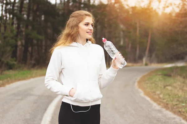 Szomjas nő. Portré, fiatal és gyönyörű redhaired sport lány ivóvíz az úton, a parkban. Fitness nő. — Stock Fotó