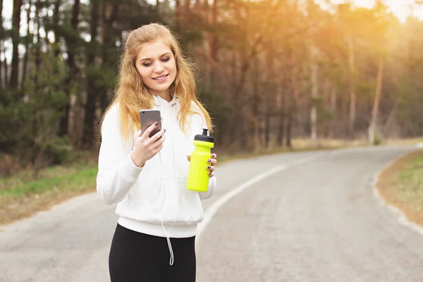 Viel Spaß beim Laufen. Porträt einer fröhlichen und attraktiven rothaarigen Sportlerin, die Musik hört, während sie das Telefon in der Hand hält. Joggen im Park. — Stockfoto