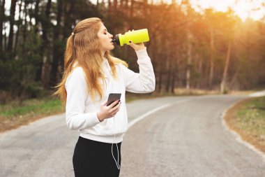Dinlenme zamanı. Park yolu üzerinde müzik dinlerken susuz genç redhaired kız içme suyu portresi.