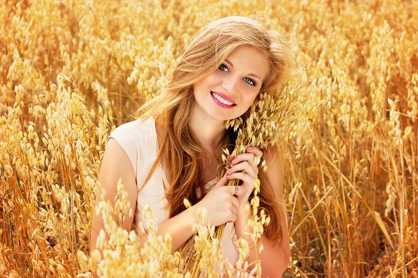 Будьте на зв'язку з природою. Портрет привабливої молодої рудої волохатої дівчини, одягненої в білу сукню, що тримає пшеницю в руках, сидячи на жовтому пшеничному полі . — стокове фото