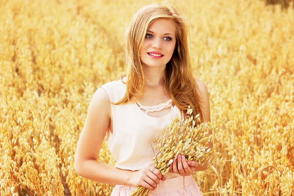 Краса сільської місцевості. Портрет привабливої молодої рудої волохатої дівчини, одягненої в білу сукню, що тримає пшеницю в руках, стоячи на жовтому пшеничному полі . — стокове фото