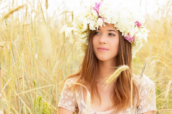 Ren skönhet. Porträtt av underbara ung kvinna klädd i vit klänning med blommor på huvudet sitter i gult vitt fält. — Stockfoto