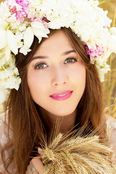 Beleza pura. Closeup retrato de bela jovem com flores na cabeça mantendo o trigo em suas mãos enquanto posando no campo de trigo amarelo . — Fotografia de Stock