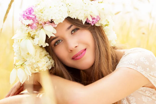 Portret piękno krajobrazów. Wspaniała młoda kobieta z kwiatów na głowie pozowanie do aparatu siedząc w polu pszenicy żółty. — Zdjęcie stockowe