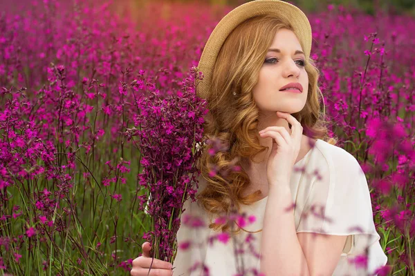 Disfruta el momento. Retrato de chica joven atractiva vestida con vestido blanco y sombrero está soñando con el futuro mientras está sentado en el prado de flores . — Foto de Stock