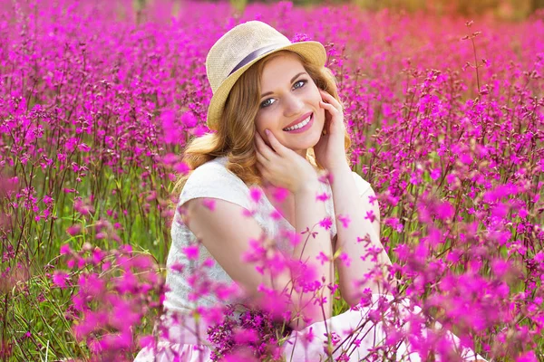 Čistá krása. Portrét krásné a atraktivní rusovláska dívka oblečená v bílých šatech a klobouk je pózuje na kameru při posezení v Květinová louka. — Stock fotografie