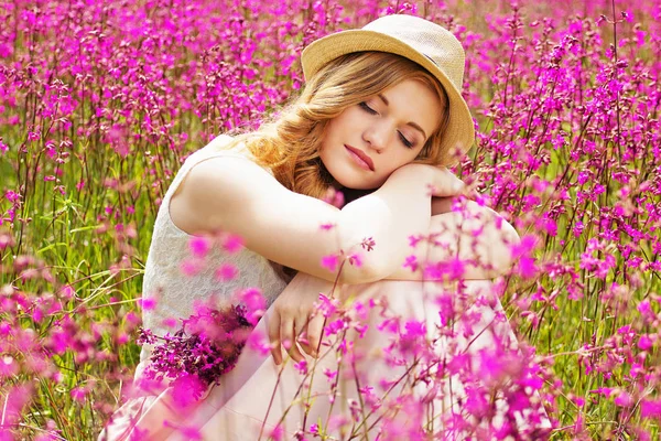 순간을 즐길 수 있습니다. 하얀 드레스 입은 매력적인 젊은 빨간 머리 여자의 초상화와 모자는 꽃 초원에 앉아있는 동안 미래에 대 한 꿈. — 스톡 사진