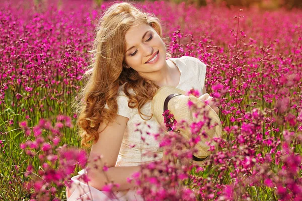 La beauté de la campagne. Portrait de jeune fille rousse attrayante vêtue de robe blanche pose à la caméra tout en se tenant dans la prairie de fleurs . — Photo