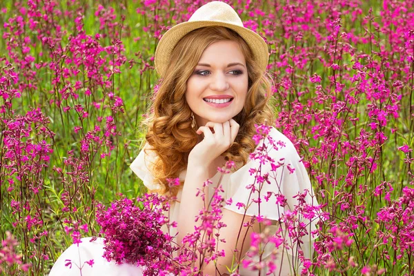 Feliz Verão. Obrigado. Retrato de bela menina vestida de vestido branco e chapéu está sentado no prado do campo de flores . — Fotografia de Stock