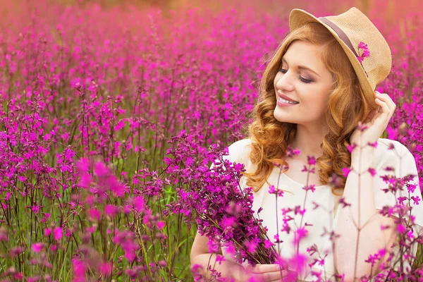 자연의 아름다움입니다. 젊은 매력적인 빨간 머리 여자의 옷을 입고 모자와 흰색 드레스 꽃 시골 풀밭에 앉아. — 스톡 사진