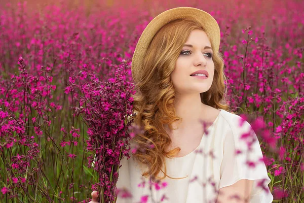 자연의 아름다움입니다. 젊은 매력적인 웃는 빨간 머리 여자의 옷을 입고 모자와 흰색 드레스 꽃 시골 풀밭에 앉아. — 스톡 사진