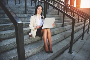 Çalışma zamanı. Güzel genç iş kadını resmi aşınmaya açık havada ofis binası yanında otururken onu laptop çalışma.