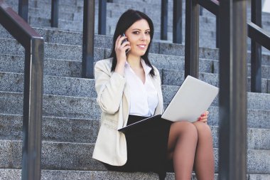 İş ortağı ile konuşma. Formal giyim ofis binası yakınındaki açık havada dizüstü bilgisayarda çalışırken telefonu konuşurken çekici emin iş kadın portresi.