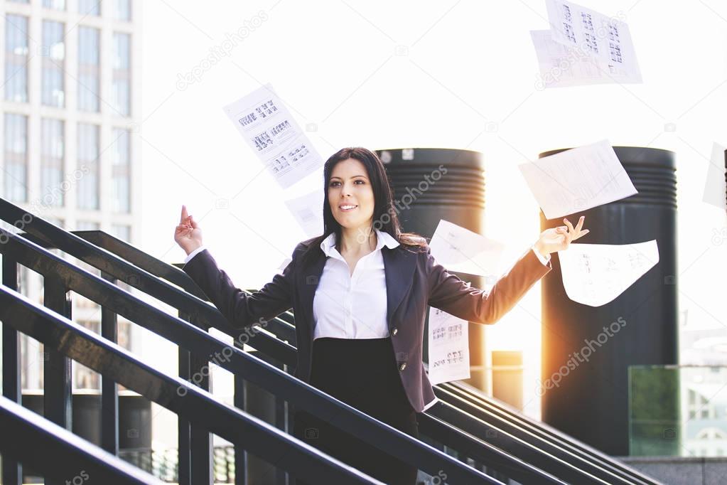 Work is done. Portrait of business woman in smart casual wear throwing paper documents away while standing outdoors against office building.