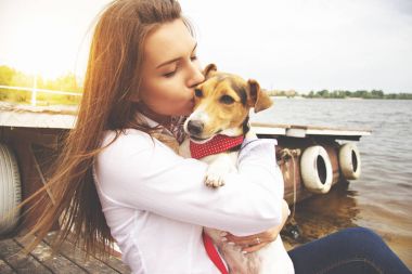 Çok güzel benim evde beslenen hayvan. Yakın çekim portre rahat kıyafetler içinde mutlu, genç ve güzel kadın küçük sevimli köpek köpek elinde tutmak ve iskelede oturup süre öpüşme.