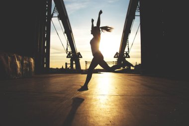 Kazanan bir kız! Arka plan üzerinde akşam gün batımı ile köprüde koşu sırasında kaldırdı silah tutan genç sportif kadın silüeti.