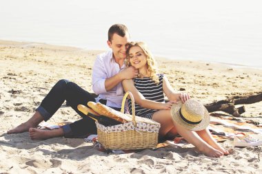 Seni çok seviyorum. Giyim gülümseyen kız arkadaşı sarılma ve sahilde piknik yaparken gülümseyen genç adam yatay çekim.