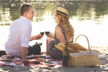 Birlikte vakit. Güzel genç çiftin şarap içme ve birbirine bakarak sahilde oturan ve piknik yaparken yatay atış.