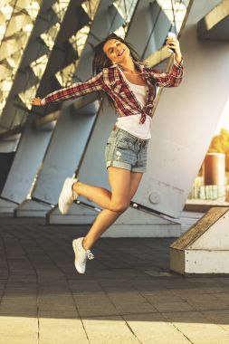 Güzellik hareket. Müzik dinleme rahat kıyafet içinde çekici genç kadın tam uzunlukta ve açık havada taşırken gülümseyen.