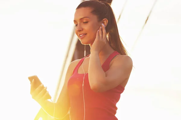 Zene a motiváció. Alacsony, szög, kilátás a gyönyörű fiatal nő, sport ruházat, használ neki telefont, és mosolyogva, miközben hallgat zenét edzés közben. — Stock Fotó
