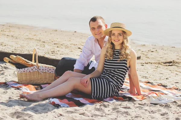 Щасливі разом. Горизонтальний знімок красивої і молодої пари, яка дивиться на камеру і посміхається, сидячи на пляжі під час пікніка . — стокове фото