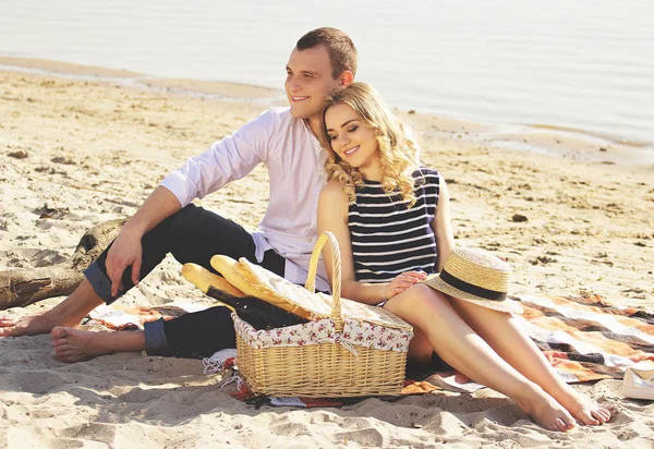 Вони у сильній любові. Горизонтальний знімок молодої і красивої пари, дивлячись далеко і посміхаючись, сидячи на пляжі і маючи пікнік . — стокове фото
