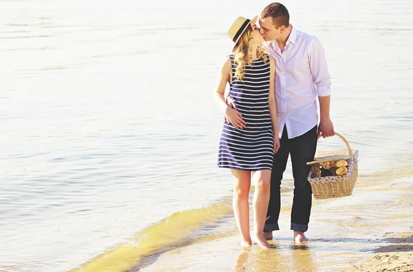 Promenades romantiques. Plan horizontal de jeune homme embrassant sa belle petite amie et gardant le panier à la main tout en marchant ensemble sur la plage . — Photo