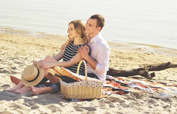 Вона моє щастя. Вид збоку чоловіка, що сидить за своєю милою дівчиною, обіймає її і посміхається, сидячи на пляжі і дивлячись в сторону. Красива пара обіймає . — стокове фото