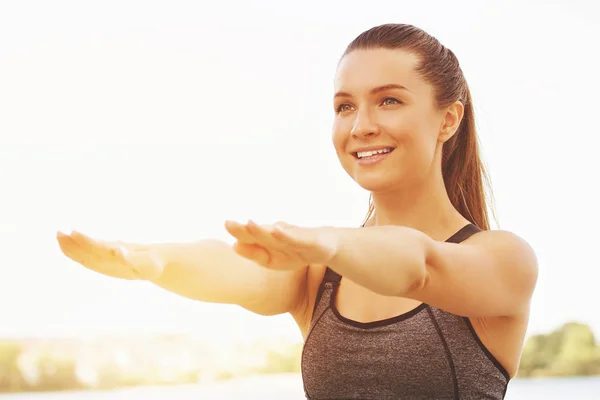 Fitness im Freien. Porträt einer schönen jungen Frau in Sportkleidung, die wegschaut und lächelt, während sie am Meer Balanceübungen macht. — Stockfoto