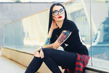 Gotik güzellik. Çekici dövmeli hippi Kız bardaklarda kentsel arka plan karşı otururken kameraya poz portresi.