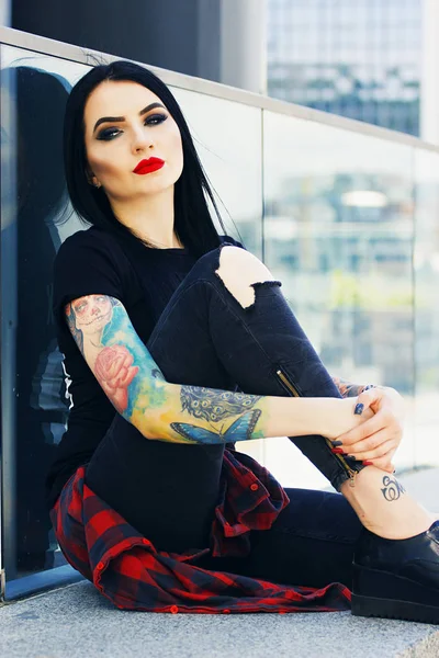 Moda de tatuagem. Retrato de menina hipster tatuado na moda com lábios vermelhos posando contra fundo urbano . — Fotografia de Stock