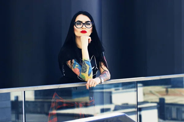 Tattoo fashion. Portrait of fashionable tattooed hipster girl with red lips posing against urban background.