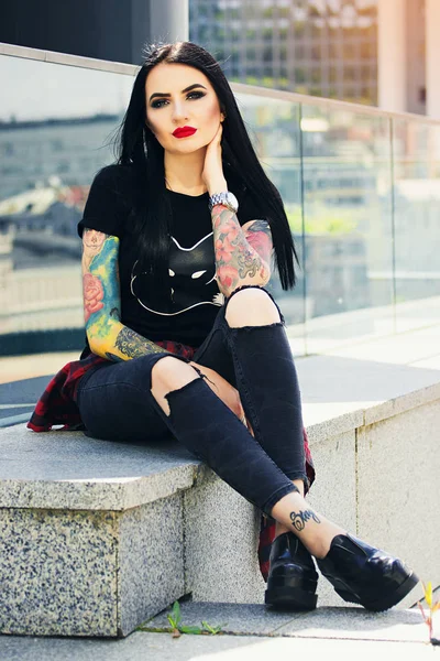 Moda de tatuagem gótica. Tiro completo de bela garota hipster tatuado posando para a câmera enquanto sentado contra o fundo urbano . — Fotografia de Stock