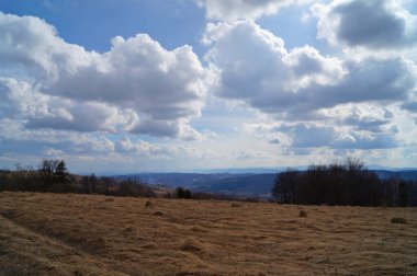 Soğuk gri gökyüzü ve ağır beyaz bulutların altında yaprakları olmayan sonbahar dağlarının manzarası.