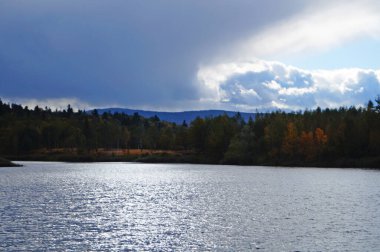 Güneşli bir günde, masmavi gökyüzünün altında, soğuk, karanlık sularla çevrili bir dağ gölü.