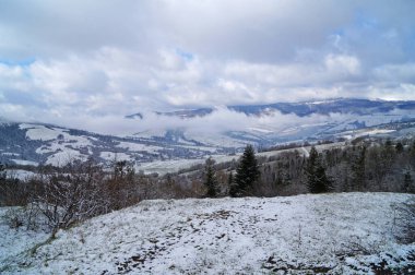 Dağ manzarası, soğuk bir kış gününde mavi gökyüzünün altında beyaz bulutlarla kaplı.