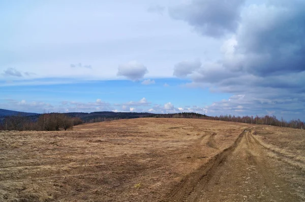 Soğuk gri gökyüzü ve ağır beyaz bulutların altında yaprakları olmayan sonbahar dağlarının manzarası.