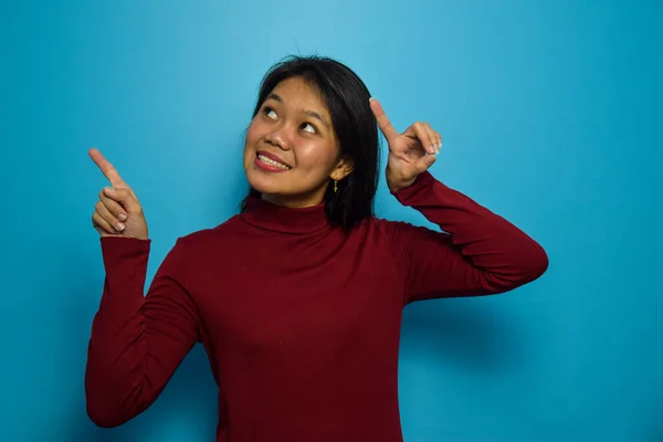 Portrait of Young beautiful asian women with blue isolated background, Pointing with two hands. Pointing gesture