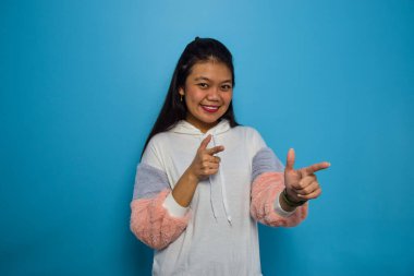 Mavi izole edilmiş geçmişi olan güzel Asyalı kadınların portresi, işaret eden ve gülümseyen