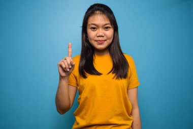 Mavi izole edilmiş geçmişi olan güzel Asyalı kadınların portresi bir numarayı işaret ederken kendine güvenen ve mutlu bir şekilde gülümsüyor.