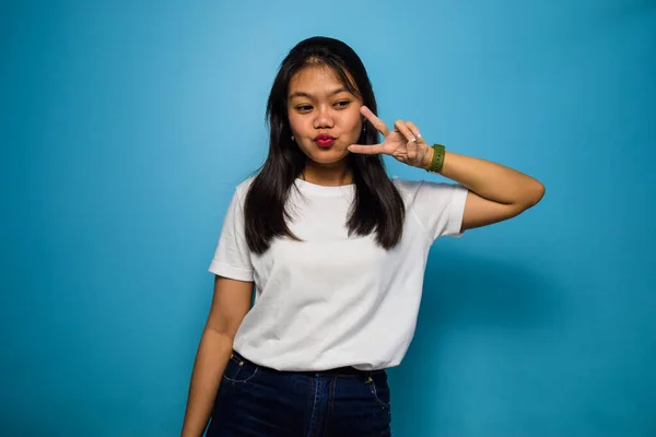 青の隔離された背景を持つ白いTシャツを使用した若い美しいアジアの女性の肖像画 平和のサインと笑顔 勝利のサイン 2つのサイン — ストック写真