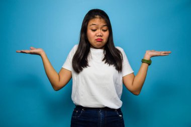 Mavi izole edilmiş beyaz tişört giyen genç ve güzel Asyalı kadınların portresi. Kameraya bakın ve kafa karıştırıcı hareketler yapın.